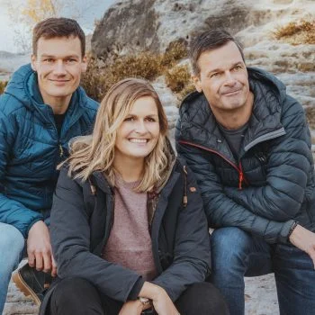 Dustin, Fanny und Thilo Mühle sitzen mit legeren Outdoorjacken bekleidet auf einem Felsen in der Sächsischen Schweiz.