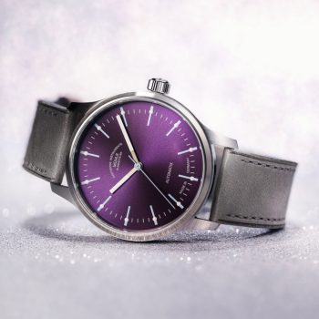 Armbanduhr Panova Violett am grauen Lederband liegt seitlich auf einem weißen Tisch.