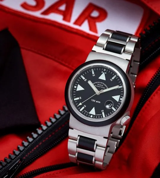 S.A.R. Rescue-Timer mit schwarzem Zifferblatt und Metall-/Kautschukband steht auf einer roten Jacke mit SAR-Aufnäher.