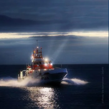 S.A.R. Rettungskreuzer fährt beleuchtet bei Nacht über das Meer.