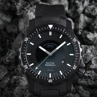 Frontalansicht der Armbanduhr Sea-Timer BlackMotion am schwarzen Kautschukband liegend auf schwarzem Gestein.