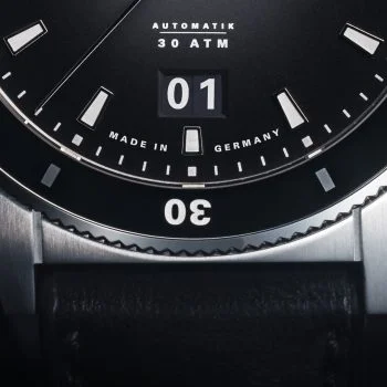 Detailbild der Armbanduhr Sportivo Großdatum mit schwarzem Zifferblatt, schwarzer Lünette und silbernem Gehäuse am schwarzen mit Fokus auf den Gehäuserand bei 6 Uhr.