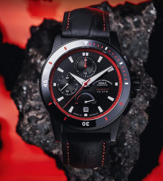 Sportivo Power Chronograph mit schwarz-rotem Lederband liegt auf einem schwarzen Stein mit roten Flächen im Hintergrund.