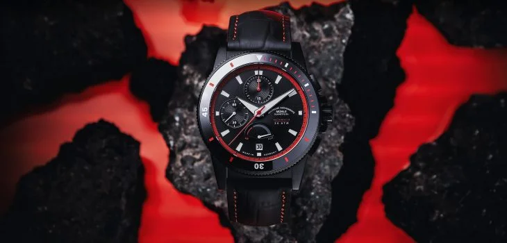 Sportivo Power Chronograph mit schwarz-rotem Lederband liegt auf einem schwarzen Stein mit roten Flächen im Hintergrund.