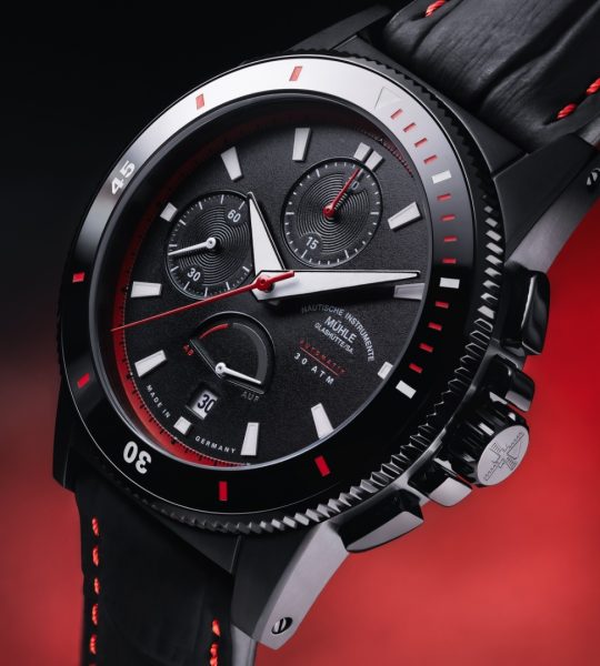 Leicht schräge Ansicht des Sportivo Power Chronograph First Edition am schwarz-roten Lederband vor rotem Hintergrund