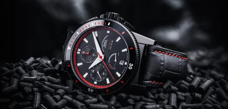 Sportivo Power Chronograph am schwarz-roten Lederband liegt seitlich auf schwarzem Granulat