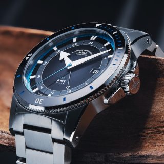 Sportivo Travel GMT mit grauem Zifferblatt und Metallband liegt über einem Ast.