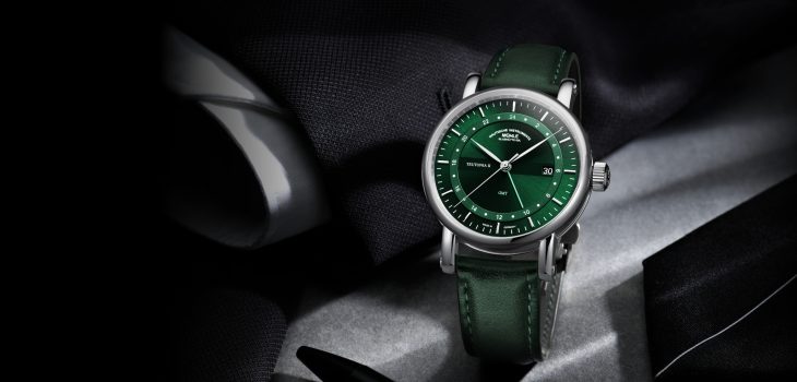 Armbanduhr "Teutonia II GMT" mit grünem Zifferblatt und Lederband steht auf grauem und schwarzen Stoff.