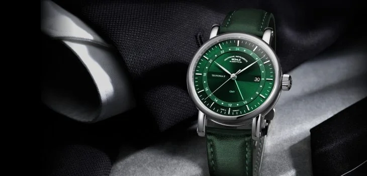 Armbanduhr Teutonia II GMT am grünen Lederband steht vor schwarzem Jacketärmel mit weißem Hemd.