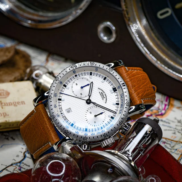 Armbanduhr Teutonia Sport I "Clous de Paris" liegt leicht seitlich zwischen einer Landkarte und Autobauteilen.