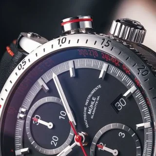 Teutonia Sport I: Nahaufnahme des rot markierten Startdrückers an einer Armbanduhr mit schwarzem Zifferblatt und silbernem Gehäuse.