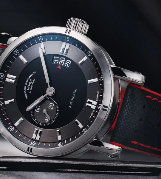 Teutonia Sport II: Armbanduhr mit schwarzem Zifferblatt, einem Hilfszifferblatt, silbernem Gehäuse und schwarz-rotem Band liegt seitlich auf einer dunklen Oberfläche.