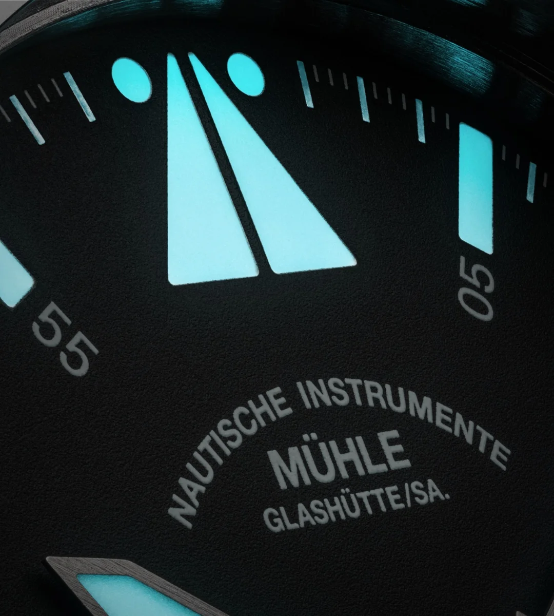 Nahaufnahme des blau-grün nachleuchtenden Fliegerdreiecks mit Punkten des S.A.R. Mission-Timers. Darunter das Mühle-Glashütte Logo vom Zifferblatt.